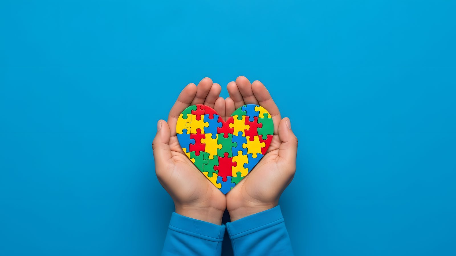 Hands holding a colourful jigsaw puzzle heart, symbolising autism and learning disability awareness